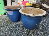 Two blue glazed planter pots shown angled side by side on a pebbled surface outdoors.