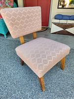 Front-side view of pink upholstered mid-century chair showing geometric pattern and wooden legs.