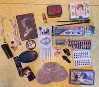 Full top view of vintage box contents showing diverse collection of small antique and vintage items laid out on yellow cloth background including sewing kits, hat pins, dressing boxes, compacts and a purse.