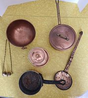 Overview of collection including large copper bowl, copper pan with lid, perforated ladle, and candle snuffers.
