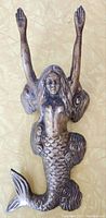 Front view of the vintage brass mermaid bootjack showing the mermaid figure with detailed scales on the tail and arms raised.