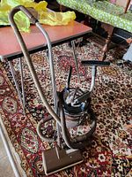 Full view of the vintage Filter Queen vacuum with attached power head, hose and metal wand on floral carpet.