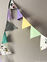 Fabric bunting triangles assembled on a wall in a draped arrangement showing various solid pastel colors and floral patterned triangles.