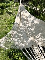 White woven cotton hammock hung outdoors with detailed view of fabric and fringe.