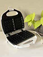 Open waffle maker showing two square non-stick waffle plates with deep waffle pattern