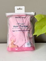 Front view of the pink microfiber hair turban in sealed clear plastic pouch with pink trimming and Spa Solutions branding
