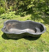 Top-down view of the black two level outdoor fish pond placed on grass, showing interior and stepped design.