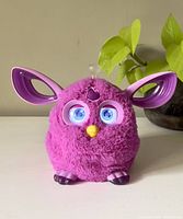 Front view of pink Furby with glowing eyes, ears up, antenna glowing, yellow beak visible.
