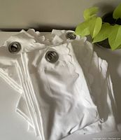 Set of three folded white curtains with visible silver metal grommets and ruffled scalloped edges.