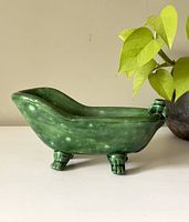 Side angle view of the green ceramic clawfoot bathtub decor showing its shape and glossy marbled surface.