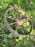Side angle view of the vintage decorative metal wheel lying on grass, showing the spokes and rusted surface.