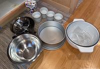 Photo of bakeware set showing ceramic ramekins, springform pan, metal strainer, stainless steel bowls, and ceramic colander with cake decorating box.