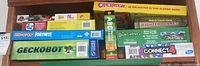 Photo showing stacked boxes of games and puzzles: Operation, ABC puzzle book, Dinosaurs floor puzzle, Connect 4, Geckobot, Build Your Own Fighter Planes, Monopoly Fortnite