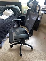 Black mesh office chair viewed at an angle showing the armrest and seat mesh.