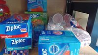Photo showing multiple boxes of Ziploc gallon storage and freezer bags, Reynolds parchment paper boxes, and packs of red Solo cups on a shelf.