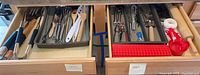 Drawer with assorted kitchen utensils including spatulas, tongs, whisks, kitchen shears, measuring spoons, and rolling pin.