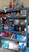 Full view of metal storage rack with various household items on shelves, blue tape visible along shelf edges
