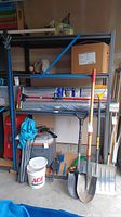 Metal storage rack with some packed items and garden tools leaning on it to show size and structure.