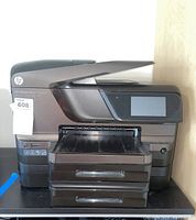 Front and angled views of the black and dark gray HP OfficeJet Pro 8600 Premium all-in-one printer showing control panel, paper trays, and document feeder.