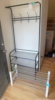 Full view of the black metal shoe and coat rack and the white framed shoe shelf on wooden floor near entrance door.