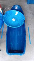 Photo showing the blue plastic sled with attached pull rope, textured seat area, and rectangular shape.
