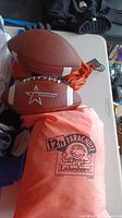 Two American footballs, hand strengtheners, and an orange carry bag for a play parachute on a white table
