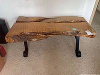 Full view of burl wood live edge table with wrought iron legs on carpeted floor.