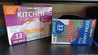 Two boxed products of Kirkland Signature trash bags: a box of 13 gallon kitchen drawstring bags with 200 count, and a box of 33 gallon extra large drawstring bags with 90 count.