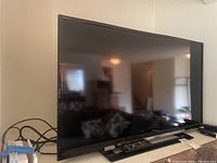 Front angled view of black Sony KDL-40R450A 40-inch LCD TV with remote on stand, reflective screen showing room behind.