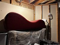 Photo of a small red modern curved couch with wave shape upholstery, placed on wrapped furniture in an unfinished room.