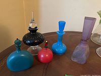 Full view of 5 art glass perfume bottles of different colors, shapes, and sizes on a wooden surface