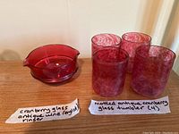 Photo of a cranberry glass antique wine rinser and four mottled cranberry glass antique tumblers behind it, showing the size and shape.