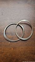 Two flat profile, irregular rounded sterling silver bangles placed on wood surface.