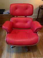 Front view of red leather lounge chair with tufted back, curved wood veneer shell and metal base.