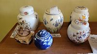 Six ginger jars and pottery pieces displayed together including floral designs, a brown artisan pottery jar, and visible cracks on the Coalport jar.