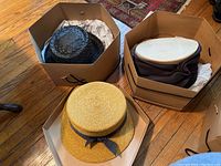 Overview of three summer hats and two brown cardboard hexagonal hat boxes on wooden floor