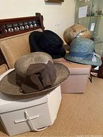 Three Lilliput summer hats placed on and around two Lilliput boxes, showing their shape, ribbon bands and bow details.