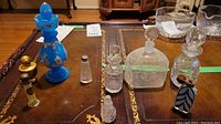 Wide shot showing eight antique and vintage perfume bottles on table including the blue handpainted bottle and clear glass bottles.