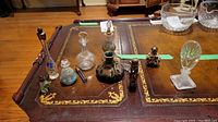 Nine assorted vintage and hand painted perfume bottles on a wooden table, various designs and materials including glass and silver overlay, some missing stoppers and with wear.