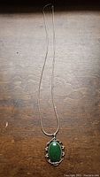 Full view of the sterling silver necklace and pendant with the jade side facing forward on a wooden surface.