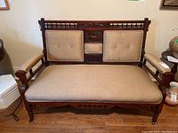Full front view of antique Victorian mahogany settee showing beige fabric cushions and the wooden frame's carvings.