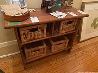 Front view of small pine wood shelf with four woven baskets in compartments. Top surface holds unrelated items not included.
