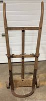 Front view of antique iron wheeled dolly showing wooden frame, vertical handles, chain, and wooden base.