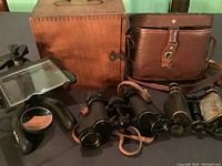 Overview showing two pairs of binoculars, microscope with magnifying visor, wooden case, and leather carrying case arranged on table