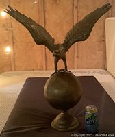 Front view of brass eagle on globe with can for scale