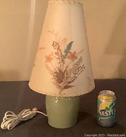 Full view of the Dornbusch lamp with light green pottery base, the floral fabric lampshade, and power cord.