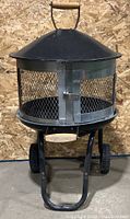 Full front view showing the outdoor fireplace with the dome lid, mesh sides and wooden handle.