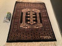 Full view of the hand knotted silk mat with geometric and floral design and fringe showing scale with adjacent can of tea.