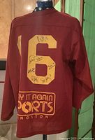 Back view of maroon hockey jersey with gold number 16 and black marker signatures from Canadian women's hockey gold medal team members.
