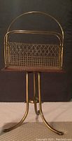 Front view of the Mid Century magazine rack showing the gold-toned metal wire geometric pattern and wooden base on tripod legs